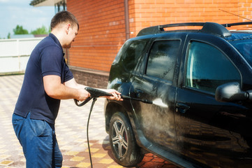 Man washing his car under high pressure water outdoors.