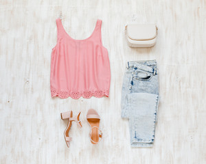 Wall Mural - Pink tank top, blue denim jeans, pink block heeled sandals and small white bag on white wooden background. Woman's casual day outfit. Trendy spring summer look in pastel colors. Flat lay, top view.