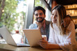 © NDABCREATIVITY - Young couple is working in cafe on laptop and smiling.