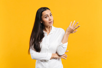 Portrait of perplexed bewildered young woman in white casual shirt looking camera, spreading hand isolated on yellow orange wall background in studio. People lifestyle concept. Mock up copy space.