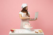 Chef cook confectioner or baker in apron white t-shirt, toque chefs hat cooking cake or cupcake at table work on pc laptop isolated on pink pastel background in studio. Mock up copy space food concept
