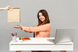 © ViDi Studio - Young smiling woman pointing hands on brown clear empty blank craft paper bag for takeaway, sit work at desk with pc laptop isolated on gray background. Achievement business career lifestyle concept.