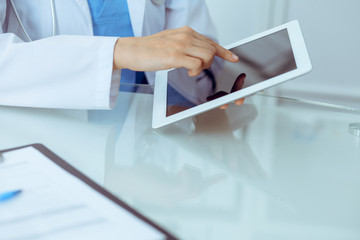 Wall Mural - Female doctor using tablet computer while sitting at the workplace, close-up of hands. Medicine, healthcare and help concept