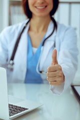 Wall Mural - Close up of female doctor thumbs up. Happy cheerful smiling brunette physician ready to examine patient. Medicine, healthcare and help concept