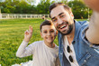 © Drobot Dean - Young man having fun with his little brother or son outoors in park beautiful green grass take a selfie by camera.