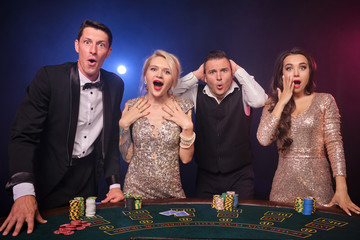 Group of a stylish rich friends are playing poker at casino.