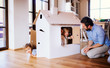 © Halfpoint - Two toddler children with father playing with paper house indoors at home.