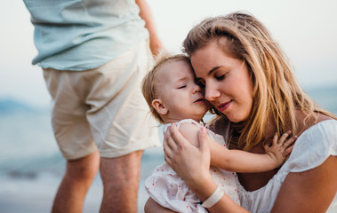 Close-up of young mother with a toddler girl on beach on summer holiday.