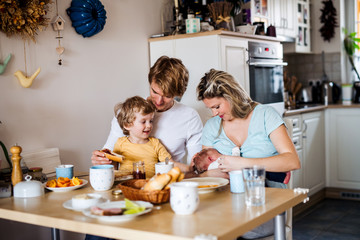 Wall Mural - Young parents with newborn baby and small toddler son at home.