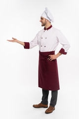 Wall Mural - Full length of smiling young cook in uniform standing isolated over white background. Looking camera pointing.