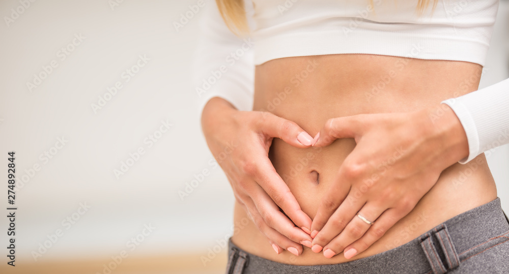 woman with sports figure on her belly shows heart shape - obrazy, fototapety, plakaty 