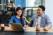 © chayathon2000 - Asian couple in blue shirt drinking coffee talking and working with computer laptop smile and  happy mood in coffee shop cafe