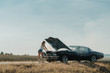 © supamotion - Young female standing near overheated car in the field, bright sunlight, steam under the hood