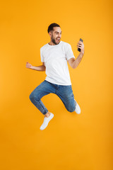 Wall Mural - Full length photo of joyful caucasian man having beard smiling and holding cellphone while jumping