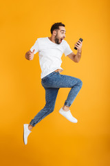 Wall Mural - Full length photo of shocked caucasian man having beard wondering and holding cellphone while jumping