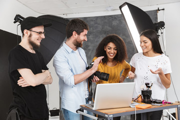 Wall Mural - Portrait of modern multiethnic people looking at laptop while photo shooting with professional camera in studio