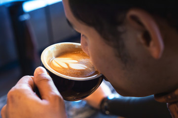 young man drinking hot coffee in a cafe with soft-focus and over light in the background