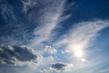 Wall Mural - white curly clouds, sun rays in a blue sky. sky background