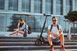 © Fxquadro - Couple of two attractive friends are chilling near glass building with their electro scooters.
