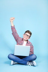 Wall Mural - Young boy with a laptop sitting on blue background