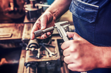 Operator working on the lathe machine and measuring the shaped material, close up photo. Concept of industry