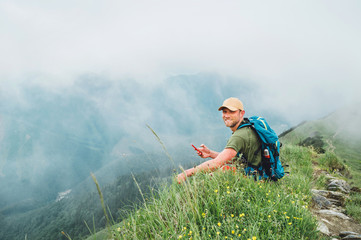 Wall Mural - tired backpacker man browsing internet using smartphone enjoying cloudy valley bottom walking by the