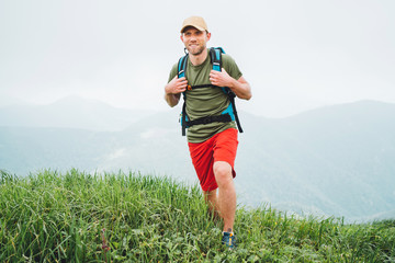 Wall Mural - tired smiling hiker man walking by the foggy cloudy weather mountain range path with backpack. activ