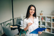 © bnenin - Portrait of a young smiling businesswoman holding file and eyeglasses, looking at camera.