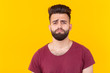 © satura_ - Sad young handsome man hipster with a beard in a burgundy t-shirt posing on a yellow background. Concept of frustration.