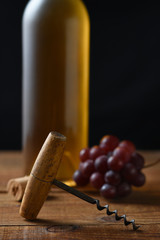 Closeup of an antique cork screw with out of focus white wine bottle grapes and cork in the background