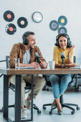 two smiling radio hosts sitting at workplace in broadcasting studio and recording podcast together