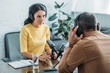 © LIGHTFIELD STUDIOS - attractive serious radio host looking at colleague while sitting at workplace in studio