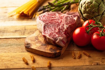 Fresh raw piece of marbled beef steak with fresh vegetables and Italian spaghetti, on a roasting board, on a wooden background.