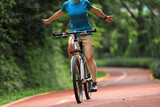 Fototapeta Na ścianę - Woman riding bike on sunny park trail with no handed