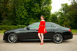 © pushann - Glamor girl in a red dress near to a business car on the background of a green park.