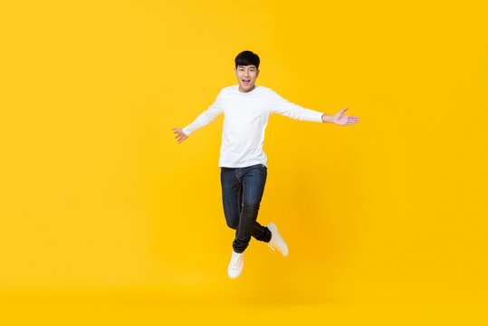 Excited asian man jumping over yellow background