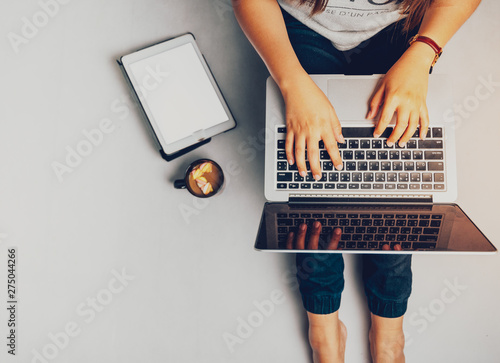 Young woman working on laptop computer while sitting on the floor and holding hot coffee, vintage tone.