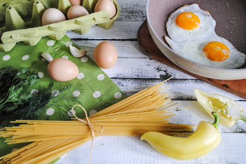 Wall Mural - Breakfast, fried eggs in a pan, spaghetti and vegetables are on the table before cooking.