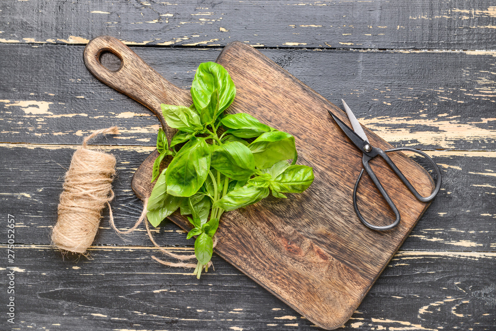 Wooden board with fresh basil, scissors and threads on table