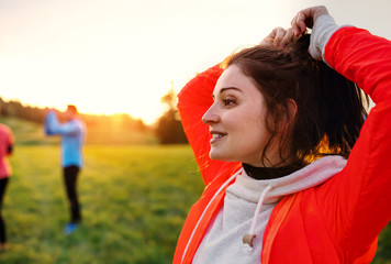 Sticker - A portrait of young woman with group of people doing exercise in nature.