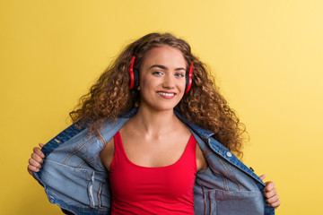 Wall Mural - Portrait of a young woman with headphones in a studio on a yellow background.