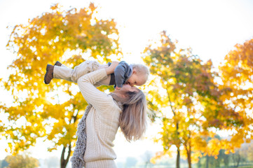 Wall Mural - Beautiful woman throws her little child up in the air in autumn park.