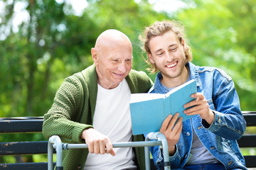 Poster - Young man reading book to his elderly father in park