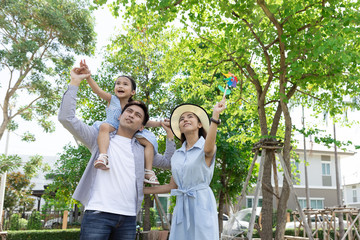 Wall Mural - Happy Asian family. Father gave his daughter a piggyback at a park at natural sunlight background and house. Family vacation concept with copy space