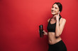 © Drobot Dean - Amazing young beautiful fitness woman posing isolated over red wall background rinking water listening music with earphones.