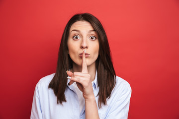 Amazing young beautiful woman posing isolated over red wall background showing silence gesture.