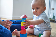 Mother With 8 Month Old Baby Son Learning Through Playing With Coloured Wooden Blocks At Home