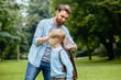© Iryna - Image of a modern beard handsome father helping his little son with backpack in the park outdoor. Back to school concept.