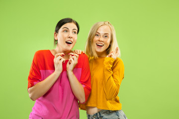 Portrait of pretty charming girls in casual outfits isolated on green studio background. Two female models as a girlfriends or lesbians. Concept of LGBT, equality, human emotions, love, relation.