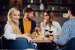 © chika_milan - Young smiling Caucasian blonde cute woman dressed smart casual sitting at table in restaurant and looking over shoulder. In background are her friends having dinner.